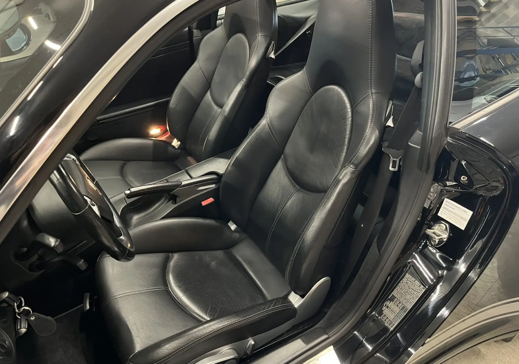 Vue intérieure côté conducteur d'une Porsche 911 Targa 997 Carrera 4S noire avec sièges sport en cuir noir et accoudoir central.