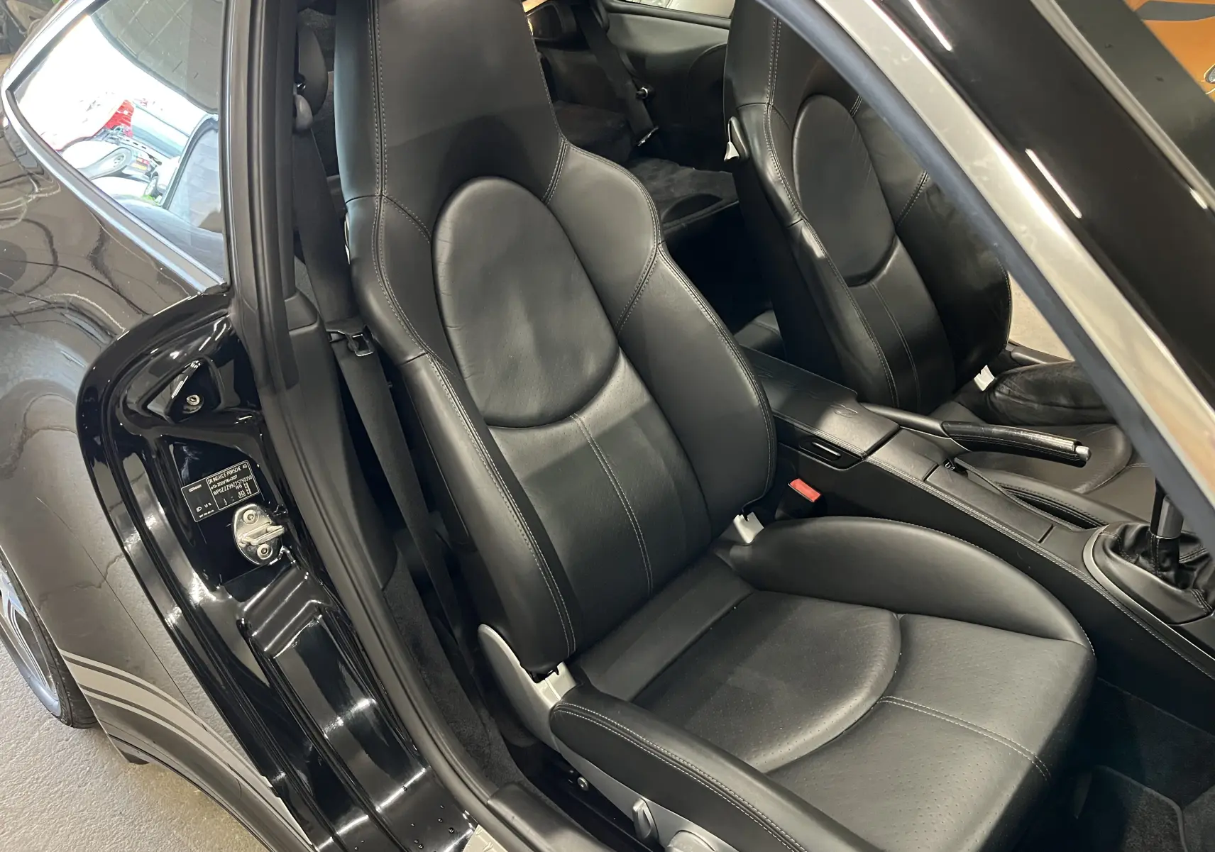 Vue intérieure côté conducteur montrant les sièges en cuir noir et la console centrale d'une Porsche 911 Targa 997 Carrera 4S noire.