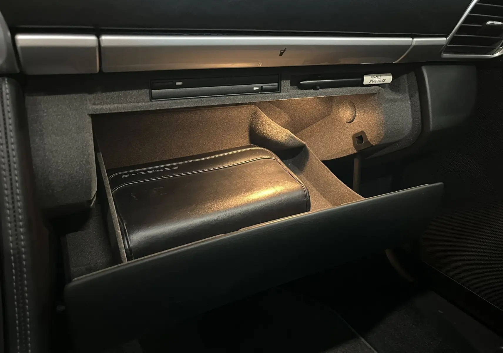 Vue intérieure sur la boîte à gants ouverte de la Porsche 911 Targa 997 Carrera 4S avec pochette cuir noire Porsche.