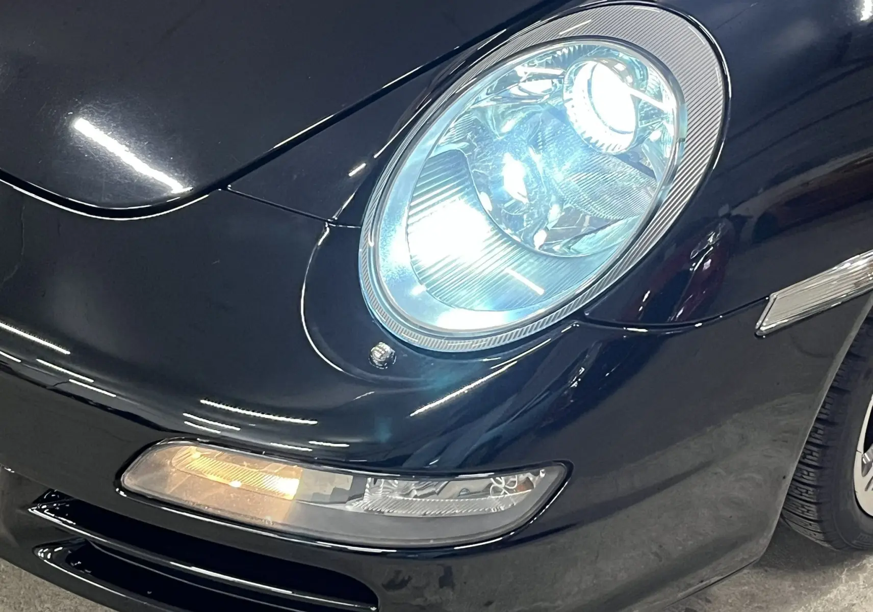 Gros plan sur le phare avant droit allumé d'une Porsche 911 Targa 997 Carrera 4S noir métallisé.