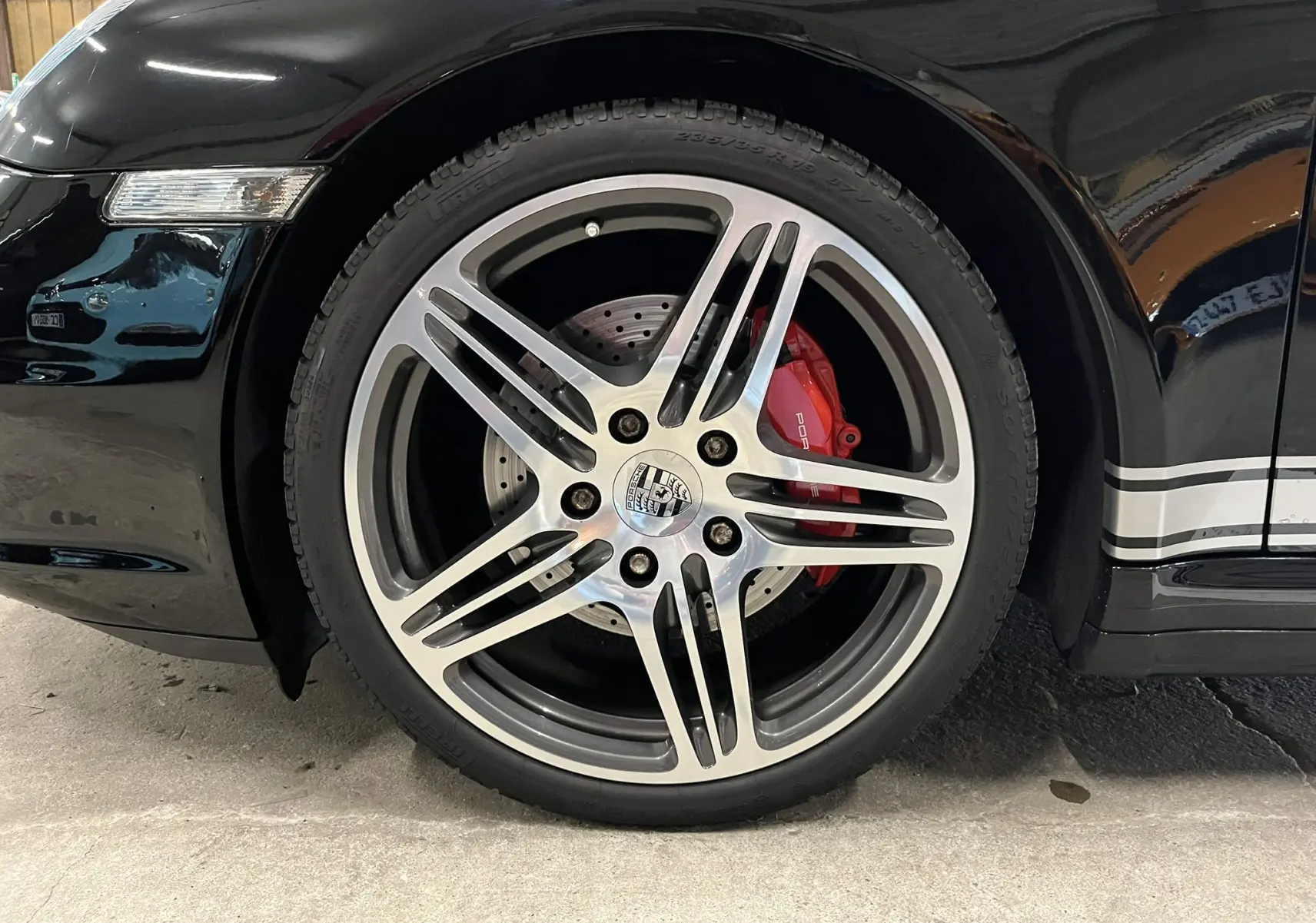 Gros plan sur la jante avant droite de la Porsche 911 Targa noire métallisée avec étrier de frein rouge et bandeau latéral argenté.