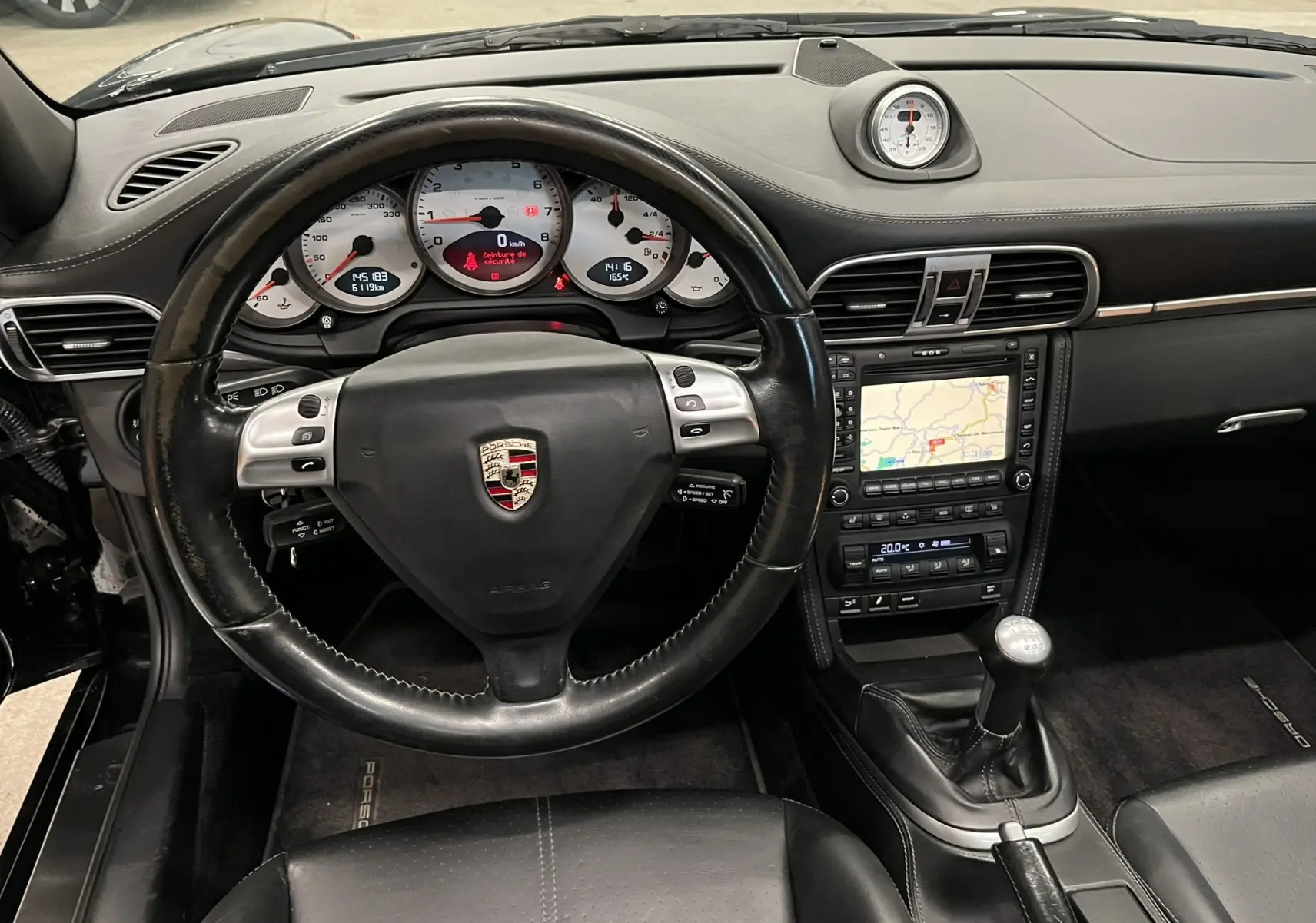Vue intérieure centrée sur le volant cuir noir et tableau de bord avec compteurs blancs et navigation GPS Porsche 911 Targa 997.