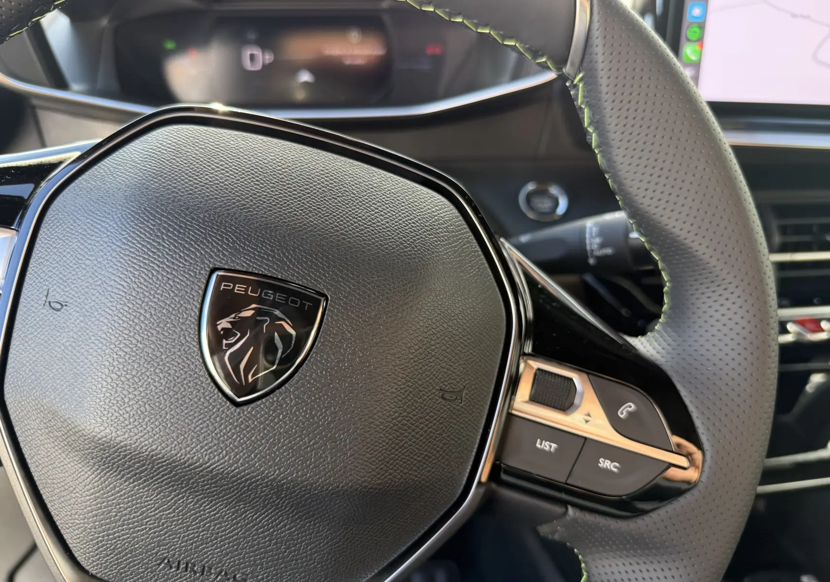 Gros plan sur le volant cuir perforé du Peugeot 2008 Hybrid 145 GT, avec logo lion et commandes intégrées à droite.