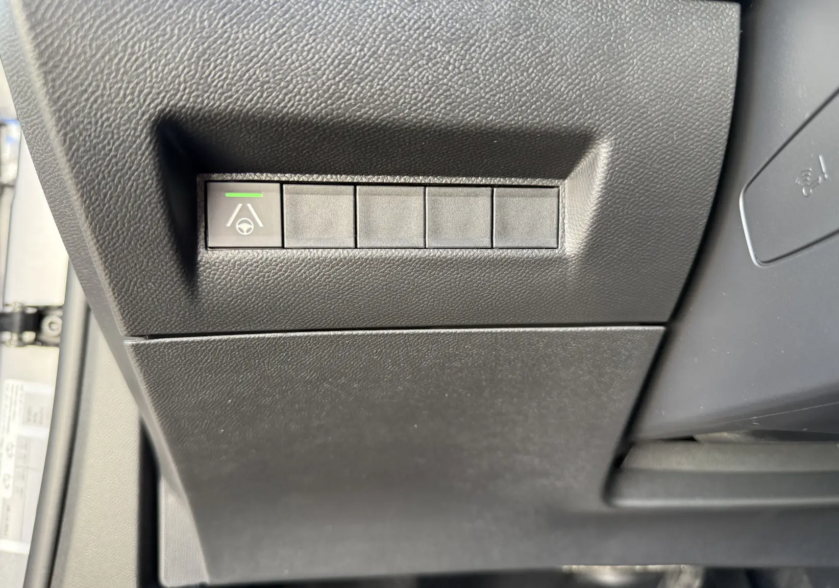 Bouton d'assistance au maintien de voie avec témoin vert sur la partie inférieure gauche du tableau de bord noir du Peugeot 2008 Hybrid 145 GT.