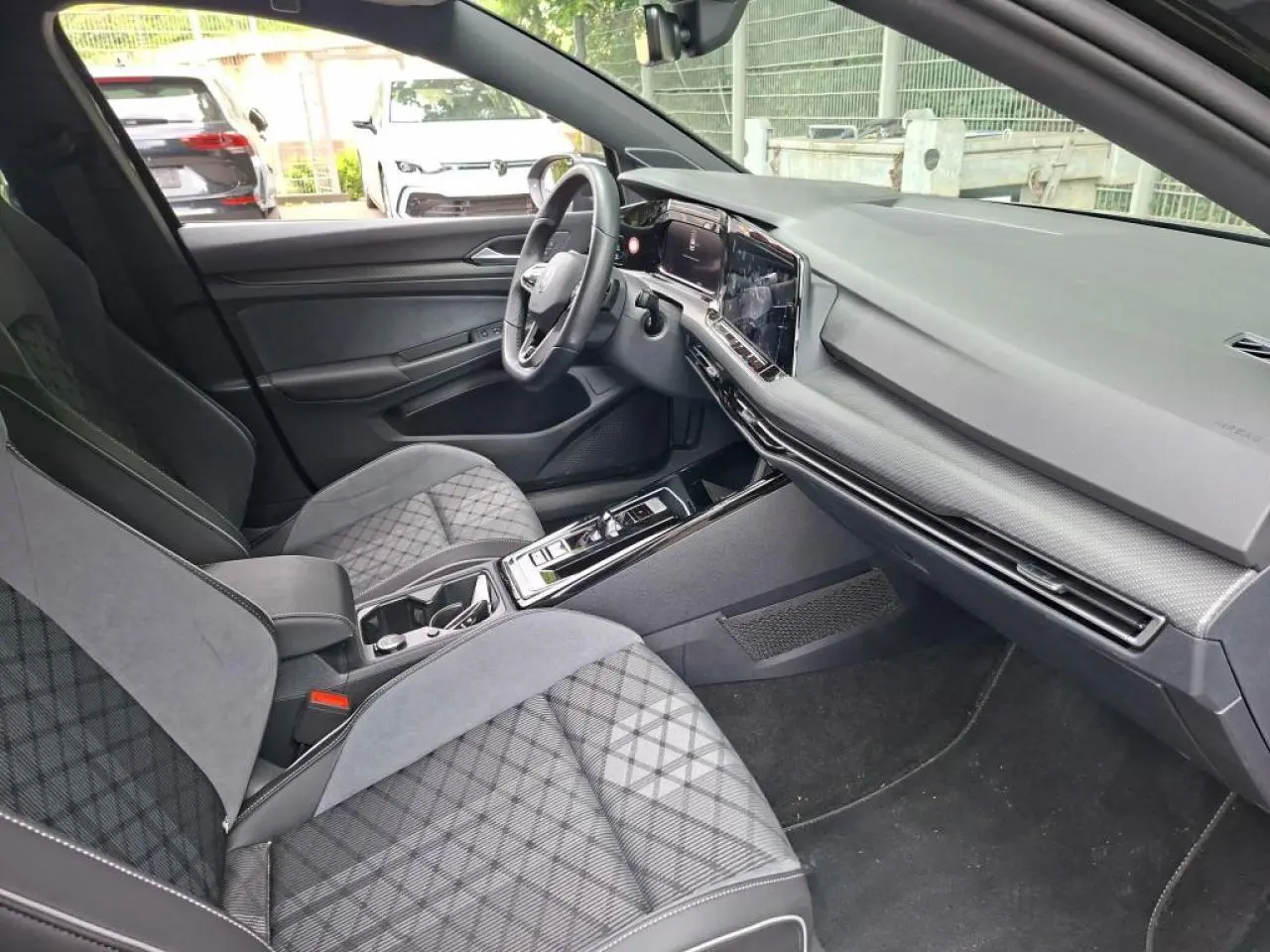 Vue intérieure côté conducteur de la Volkswagen Golf 8 R-Line 2024, avec sièges sport en tissu gris à motifs et tableau de bord moderne.
