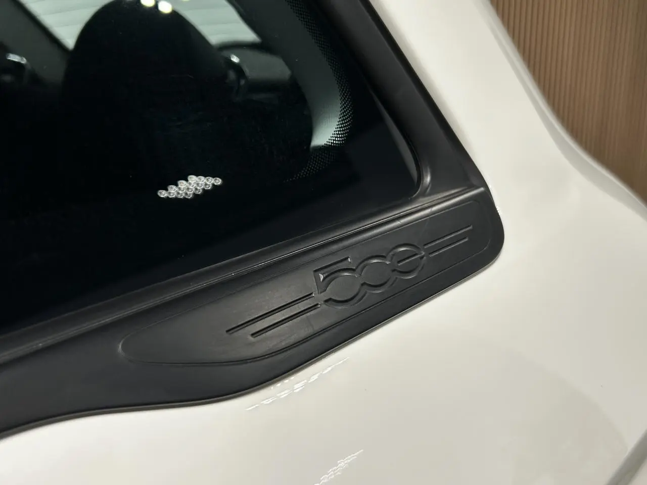 Gros plan sur l'emblème noir 500e sur la portière côté droit d'une FIAT 500 électrique blanche.