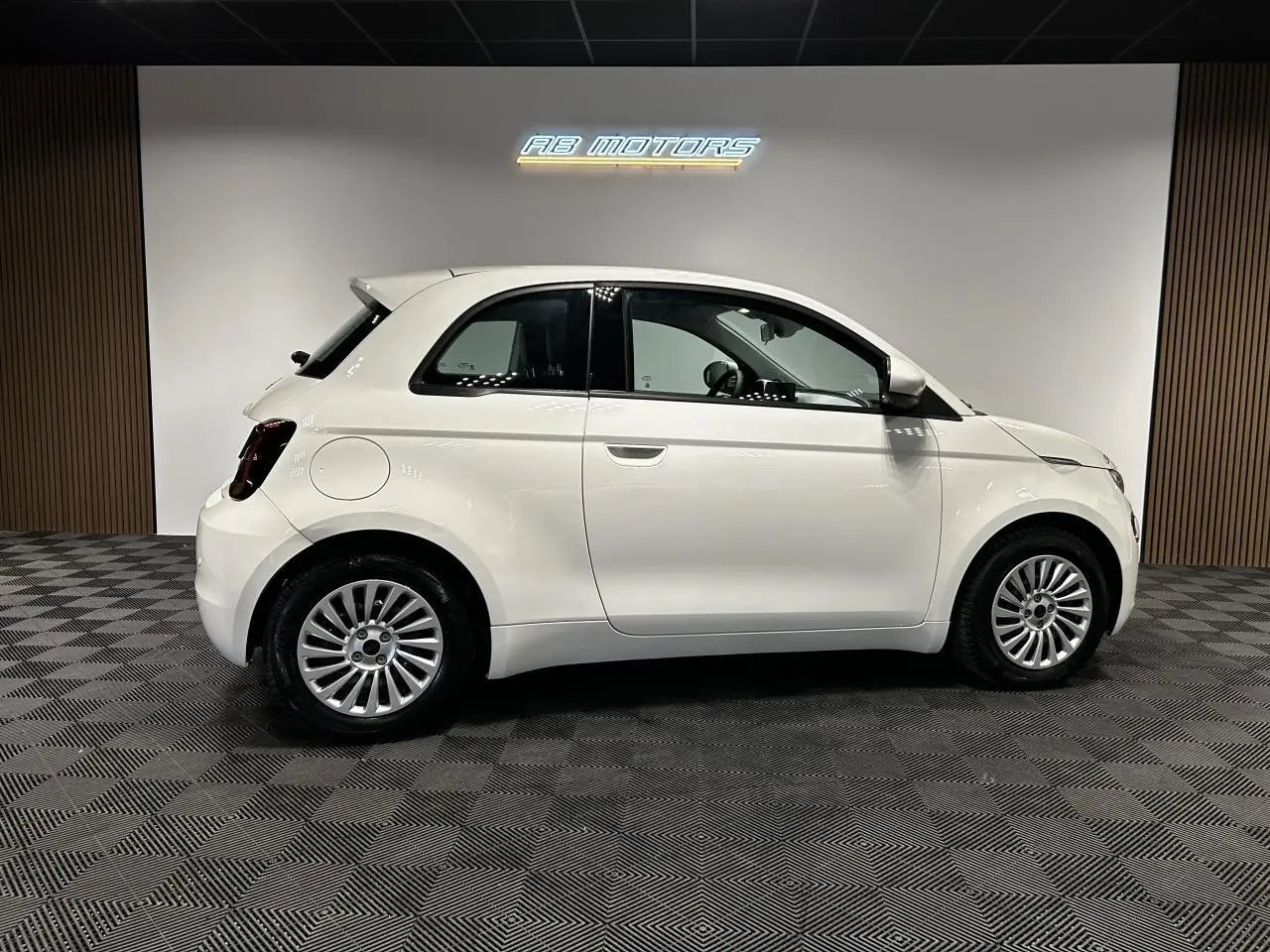 Profil droit d'une Fiat 500 électrique blanche 2024, avec jantes alliage et intérieur visible à travers les vitres.