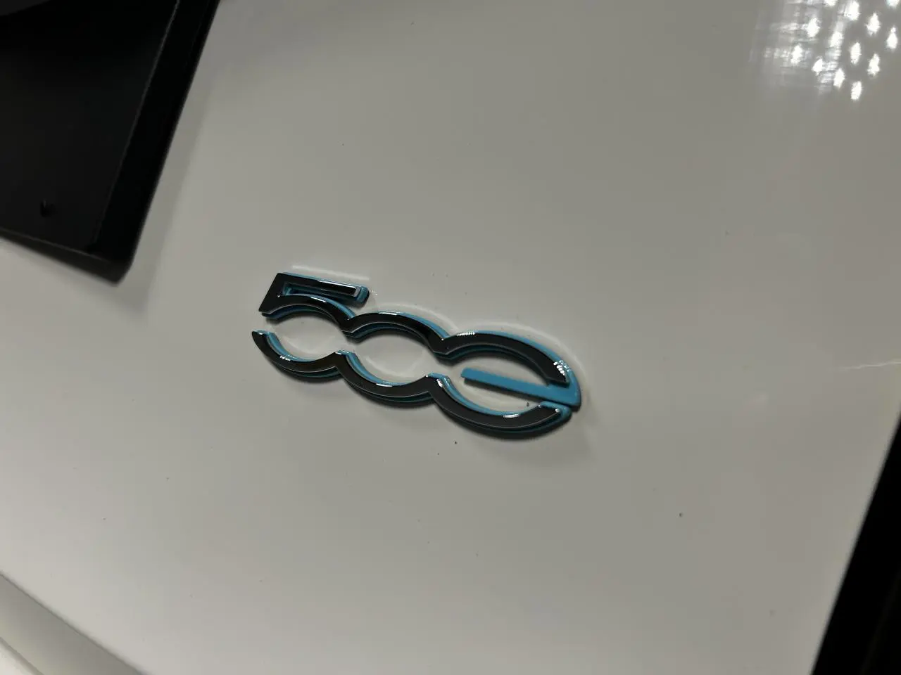 Gros plan sur l'emblème "500e" bleu et noir sur la carrosserie blanche d'une Fiat 500 électrique 2024.