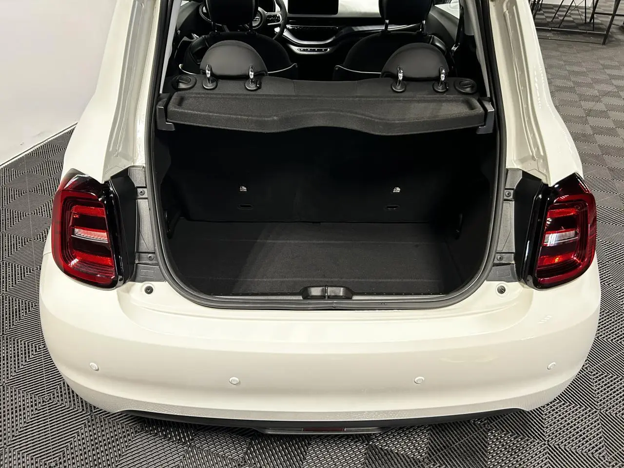 Vue arrière ouverte du coffre d'une FIAT 500 électrique blanche 2024, avec intérieur noir et feux arrière LED rouges.