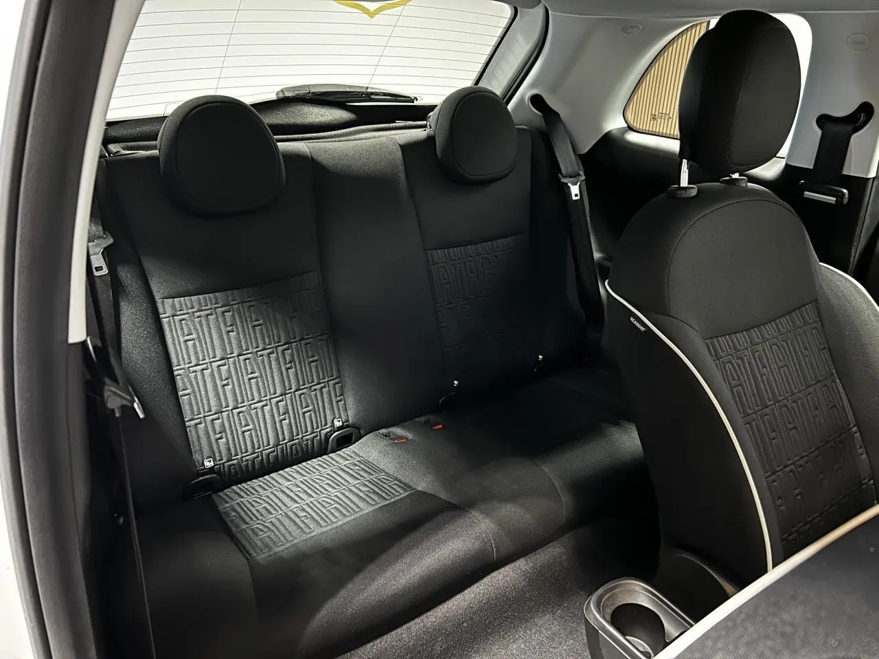 Vue intérieure arrière de la Fiat 500 2024 électrique, sièges tissu noir avec monogramme FIAT et appuie-têtes ronds.