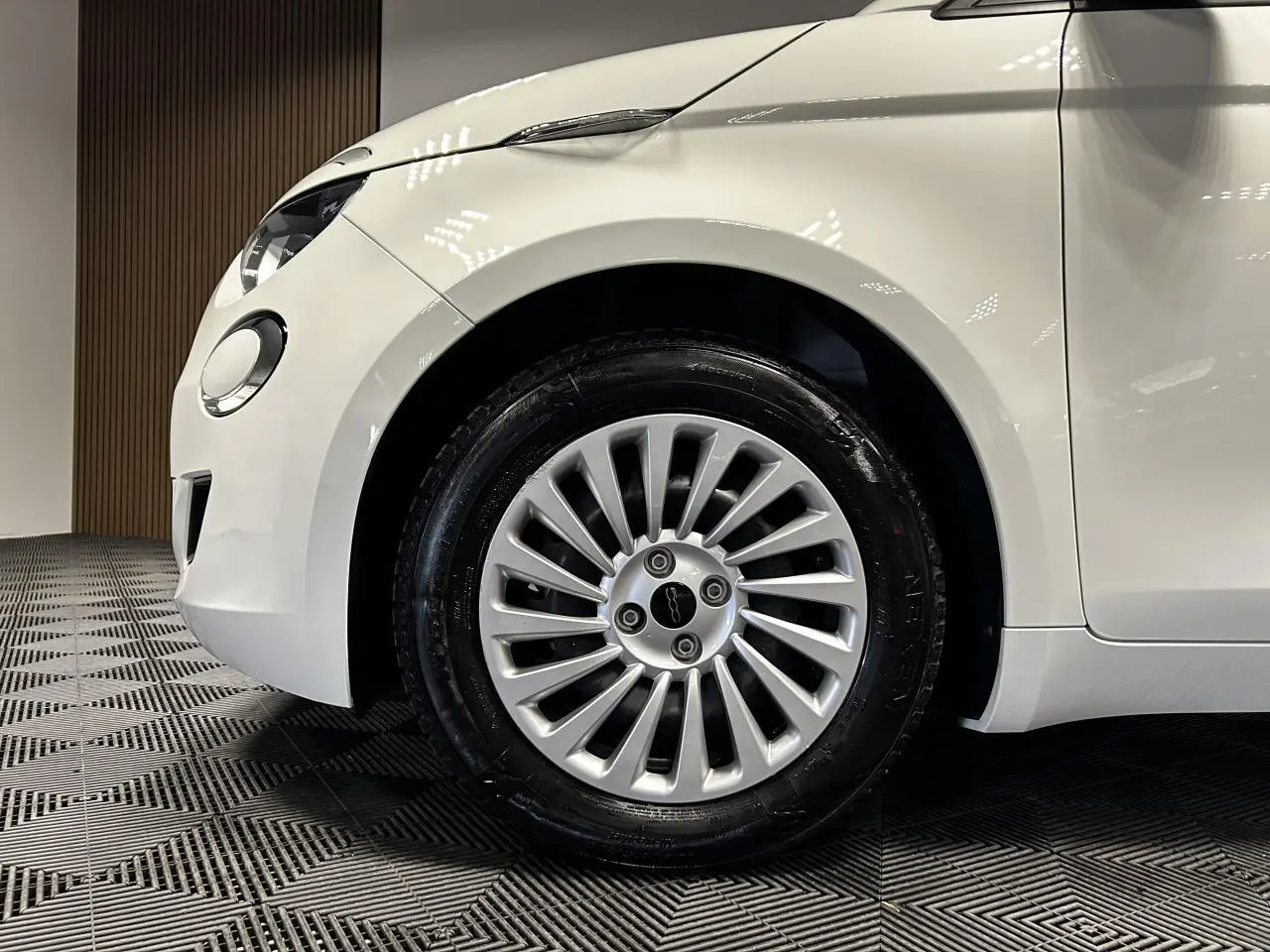 Gros plan sur la roue avant gauche et partie avant blanche d'une FIAT 500 électrique 2024 avec jante acier 15 pouces.