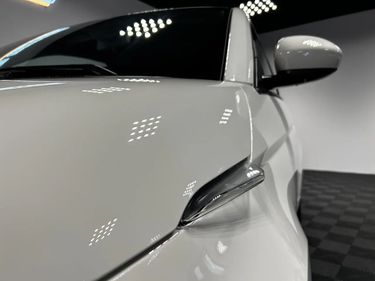 Gros plan sur le rétroviseur droit blanc d'une Fiat 500 électrique 2024 avec carrosserie lisse et reflets lumineux.