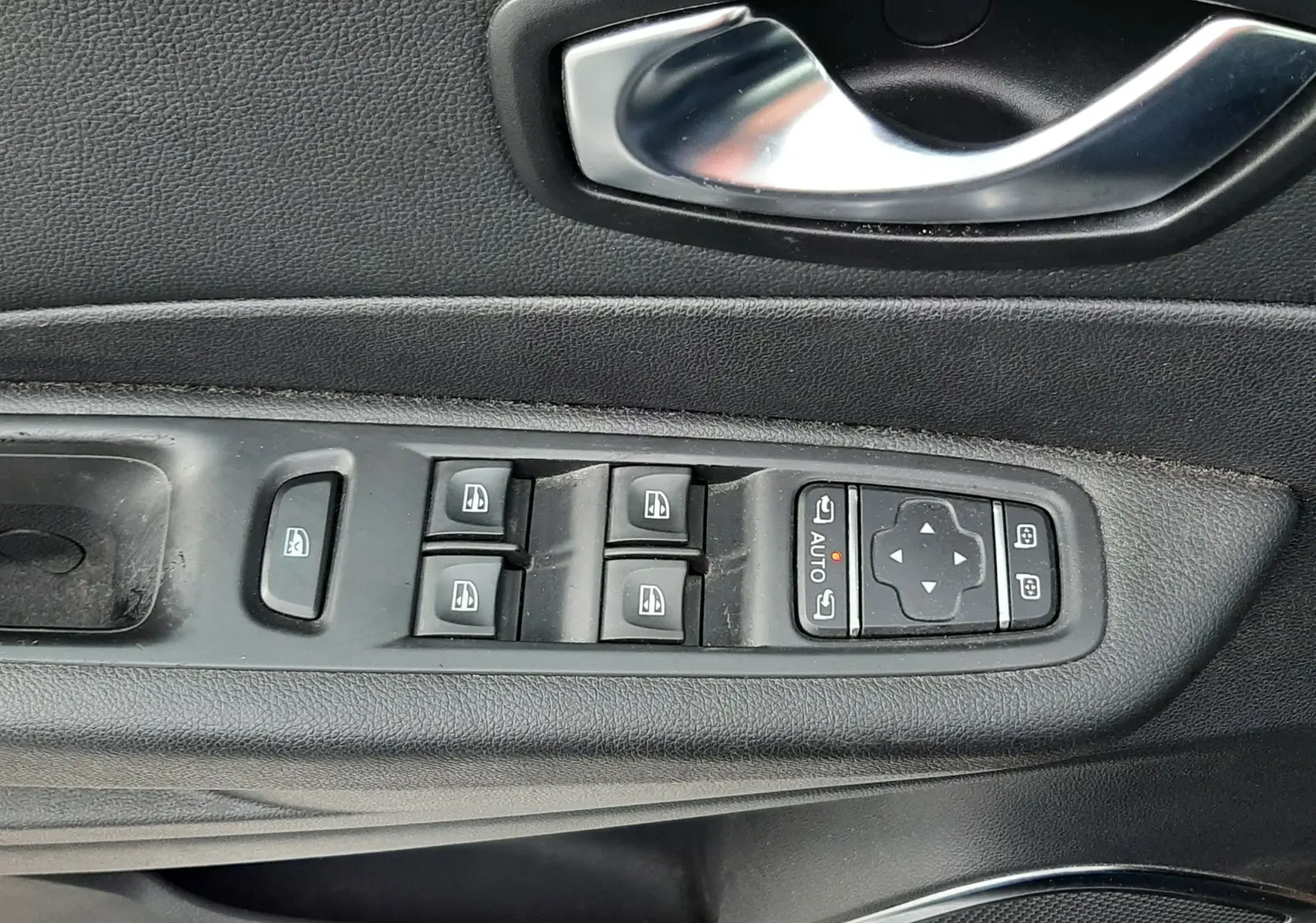 Gros plan sur la commande des vitres électriques et la poignée intérieure côté conducteur d’un Renault Captur gris toit noir.