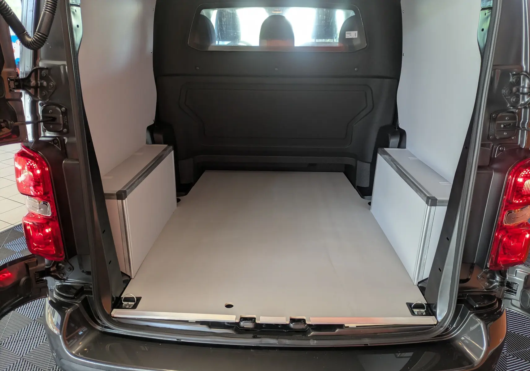 Vue arrière du Citroën Jumpy gris titane montrant l’espace de chargement avec plancher et coffrages bois blancs.
