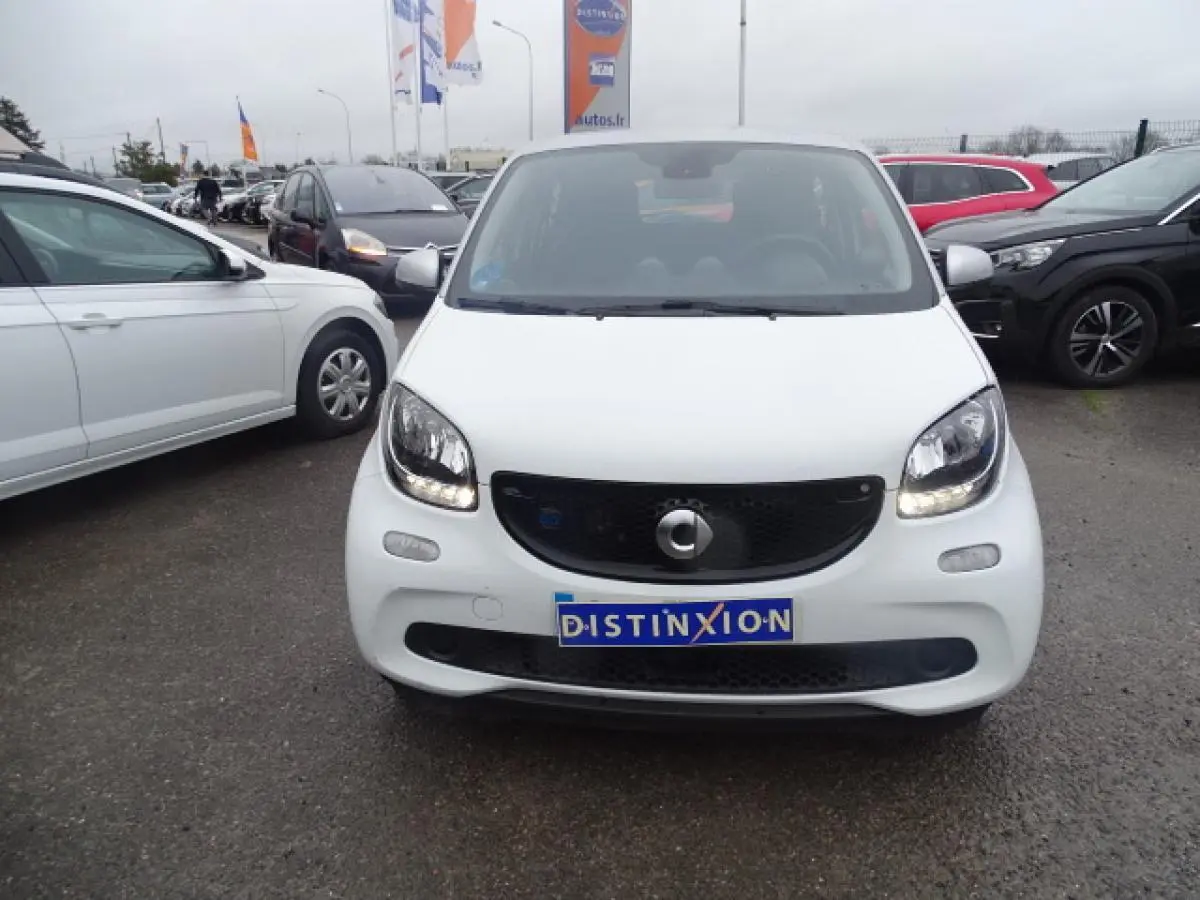 Vue avant d'une Smart Forfour Electric Drive Prime blanche avec calandre noir brillant et feux allumés sur parking.