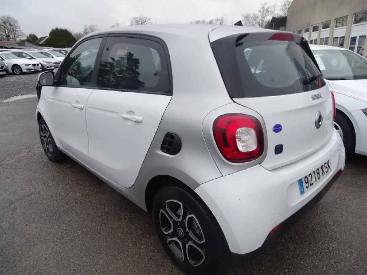 Vue 3/4 arrière droite d'une Smart Forfour électrique blanche avec jantes alliage bicolores et logo EQ sur le hayon.