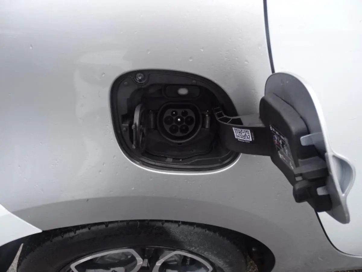 Gros plan sur la prise de recharge côté gauche d’une Smart Forfour électrique blanche, avec port ouvert au-dessus de la roue arrière.