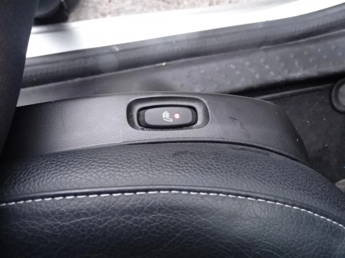 Gros plan sur le bouton de siège chauffant noir avec témoin rouge, entouré de sellerie cuir noir et plastique texturé.