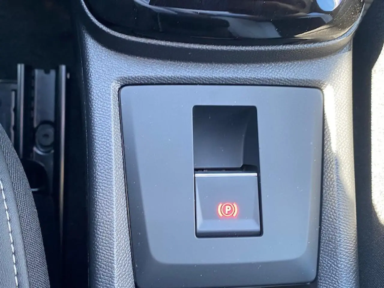 Gros plan sur le bouton de frein de stationnement électrique au centre de la console d'une Citroën C3 Aircross gris Mercury.