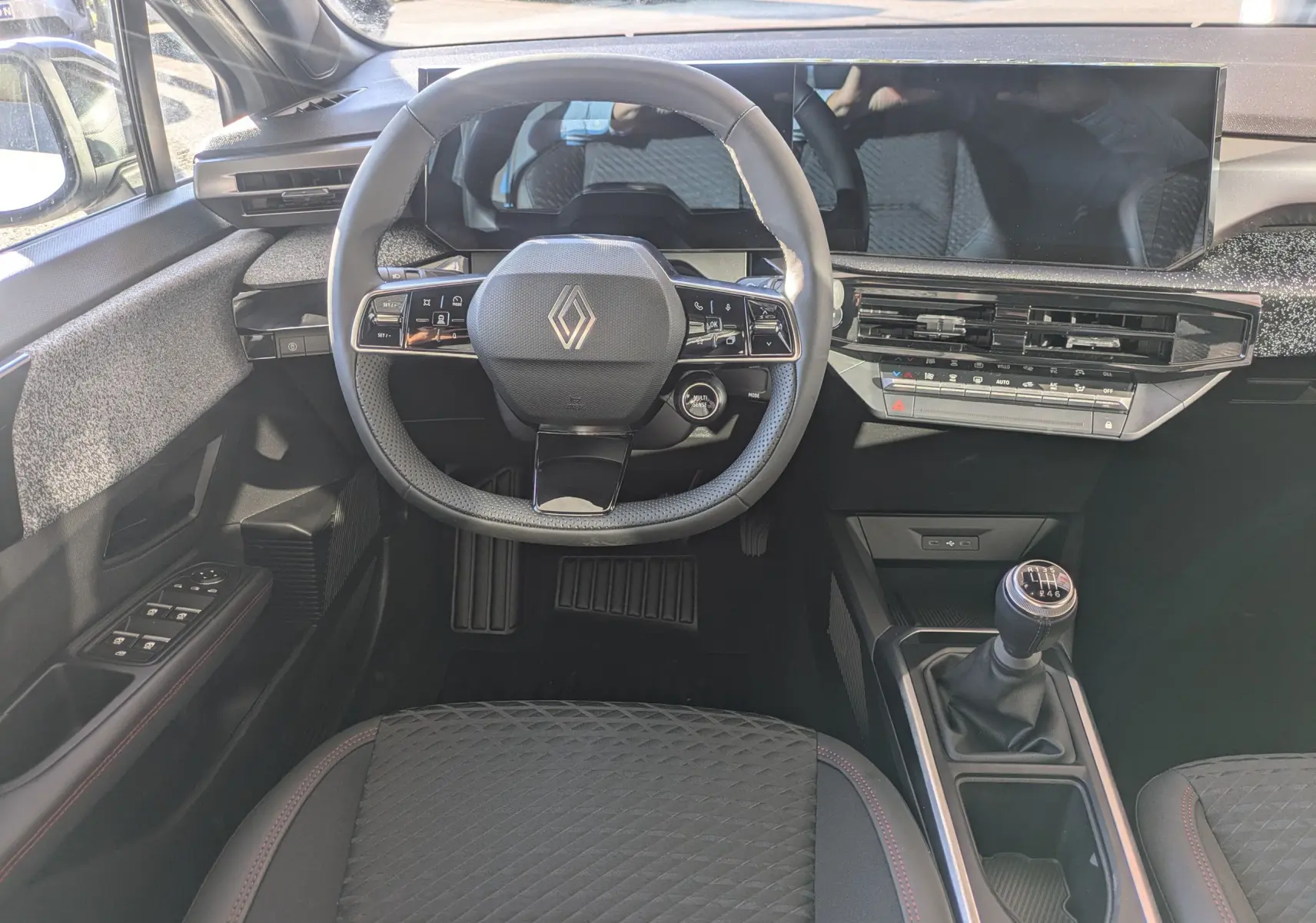 Vue intérieure frontale de la Renault Clio VI TCe 115ch avec volant multifonction, écran large et levier de vitesse manuel.