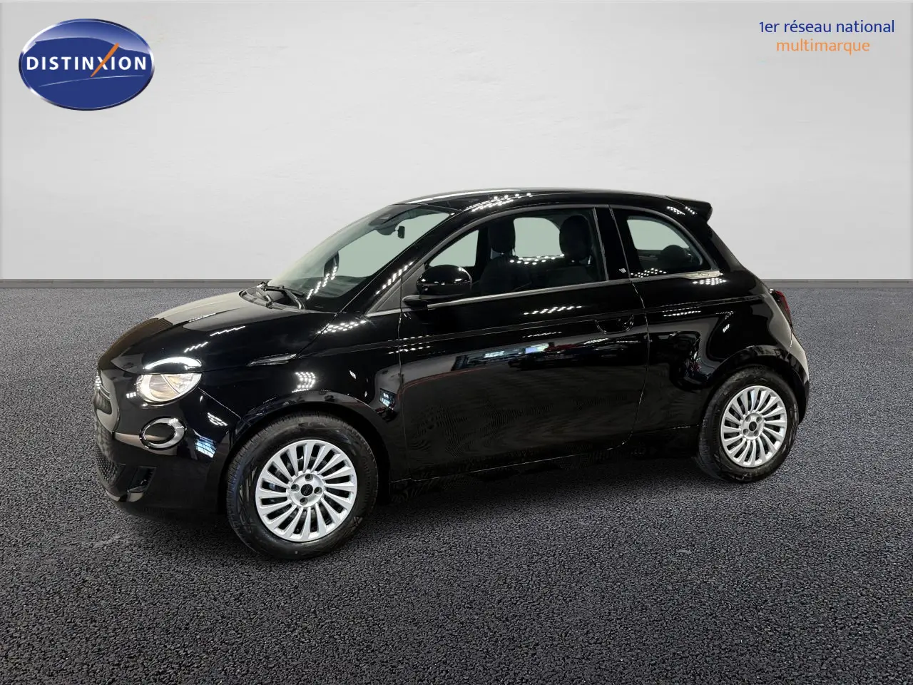 Profil droit de la Fiat 500 électrique noire 2024 avec jantes acier 15 pouces dans un showroom lumineux.