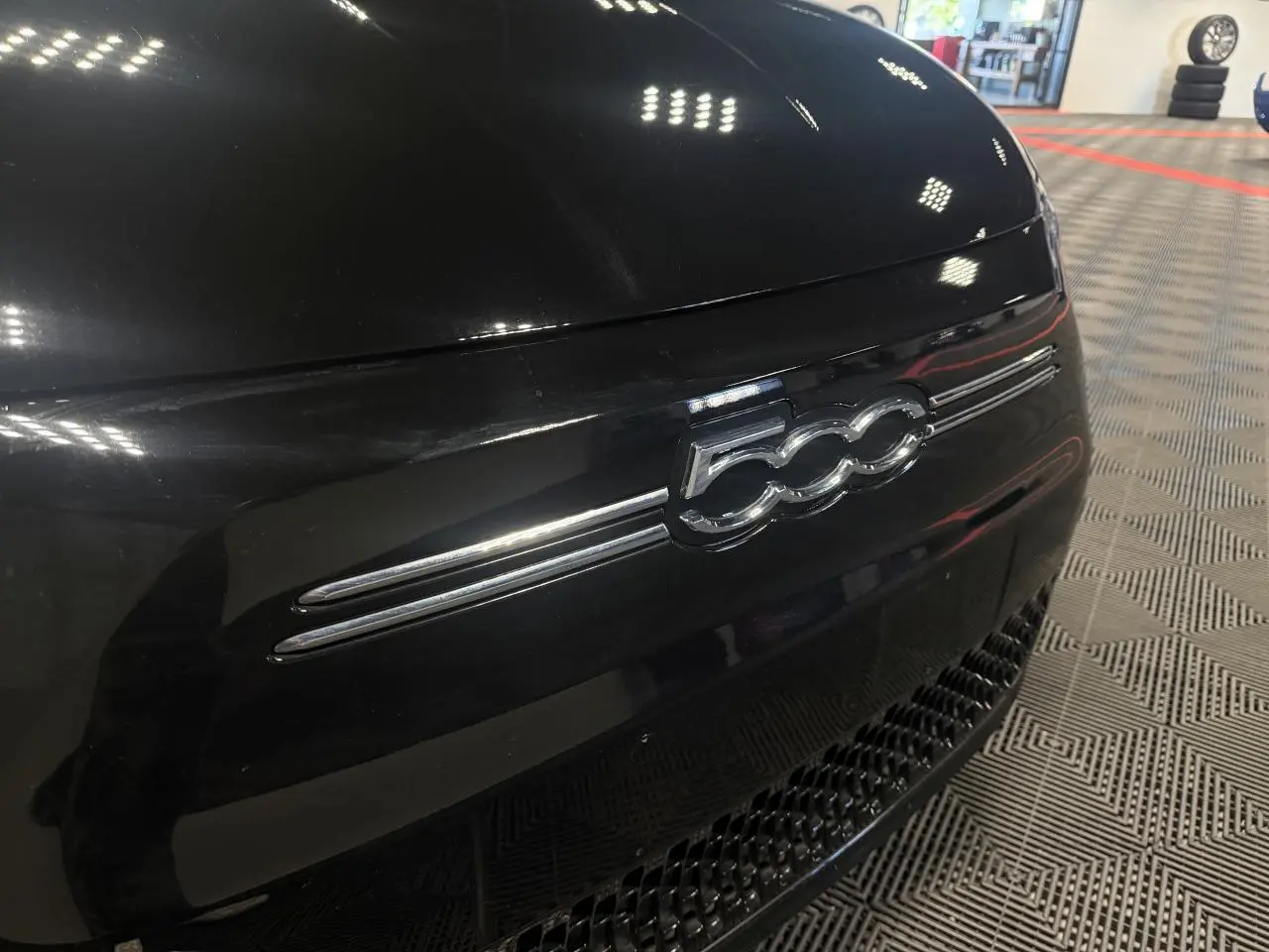 Gros plan sur l’avant noir brillant d’une FIAT 500 électrique 2024 avec logo 500 chromé et calandre inférieure ajourée.