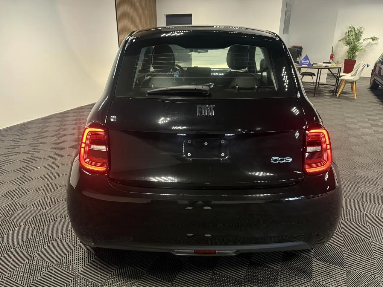 Vue arrière d'une Fiat 500 électrique noire 2024 avec feux arrière allumés dans un showroom.