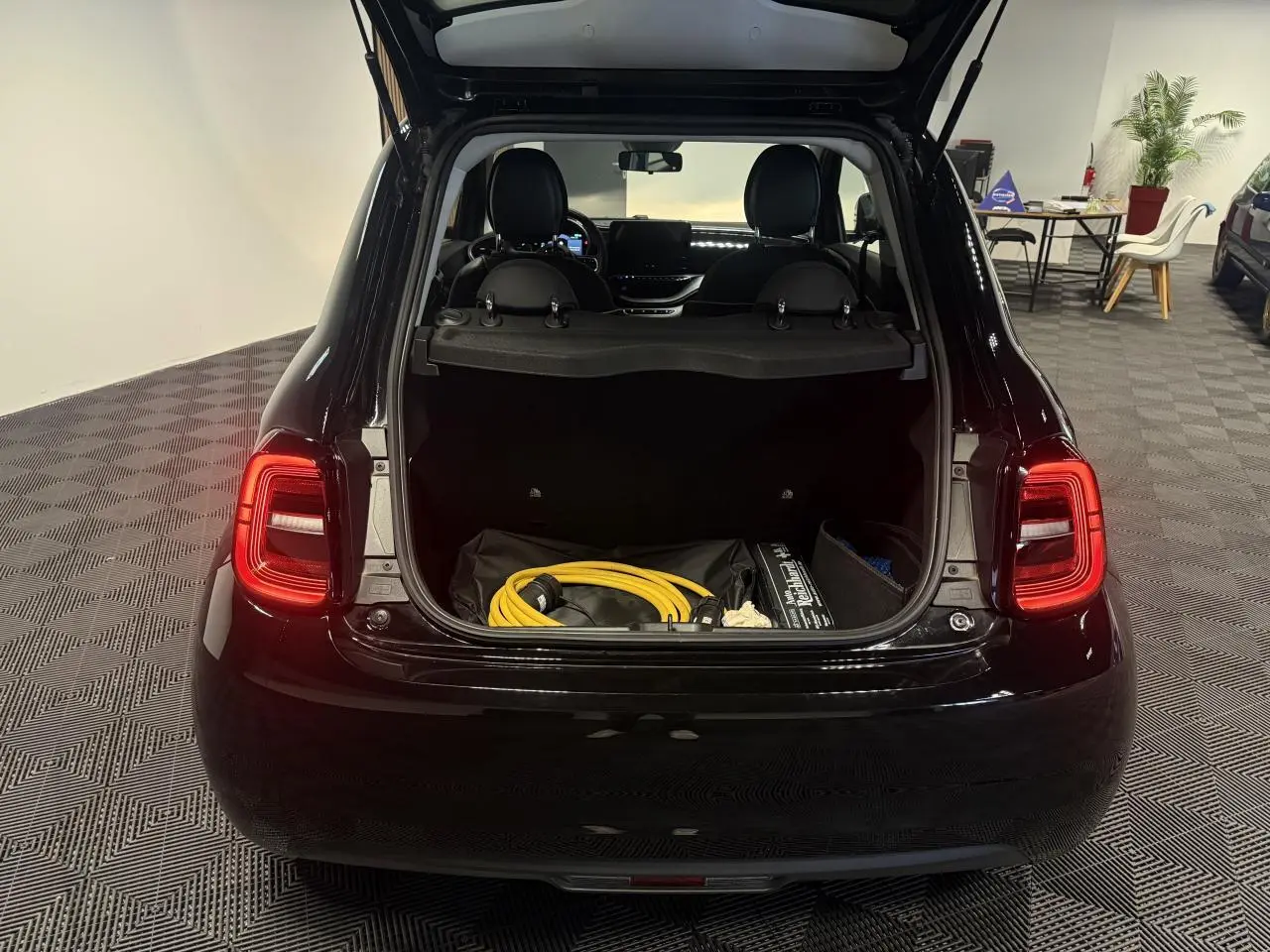 Vue arrière ouverte de la Fiat 500 électrique noire 2024, coffre visible avec câble de recharge jaune à l'intérieur.