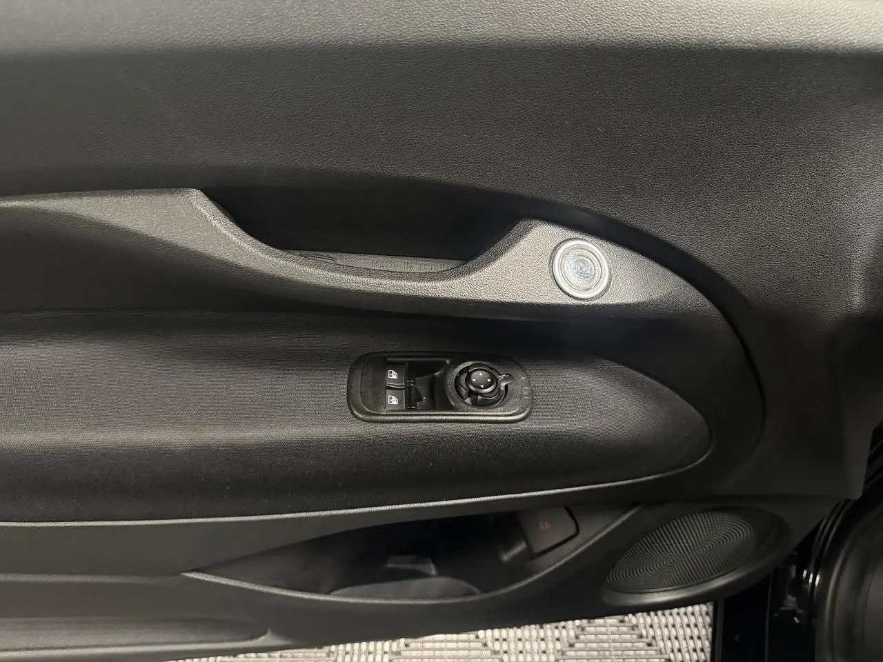 Intérieur côté gauche de la porte d’une Fiat 500 électrique noire 2024, avec commandes de vitres et haut-parleur intégré.