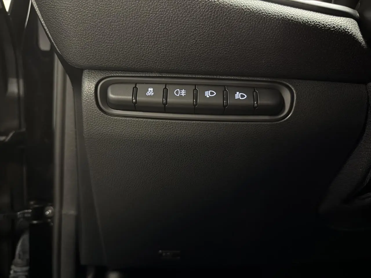 Gros plan sur les commandes de réglage des phares et aides à la conduite dans une Fiat 500 électrique noire 2024.