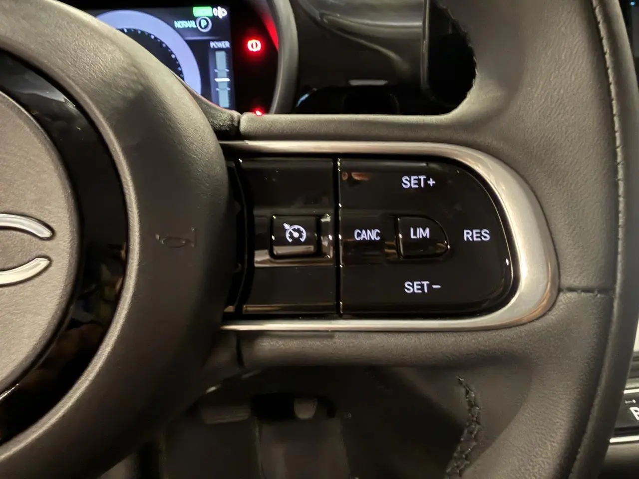Gros plan sur les commandes du régulateur de vitesse du volant noir soft-touch d'une Fiat 500 électrique 2024.