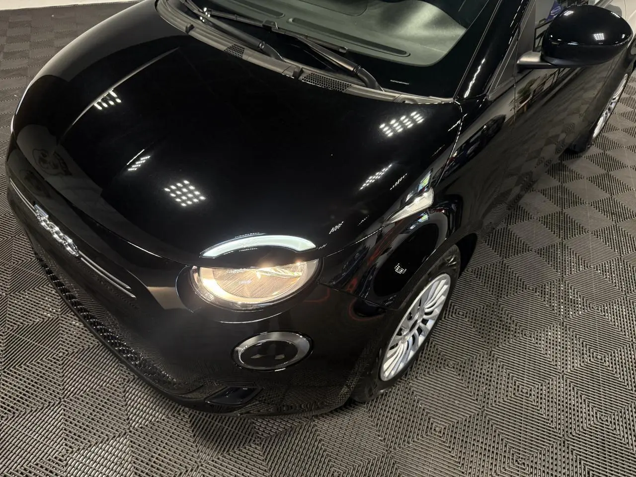 Vue 3/4 avant droit de la Fiat 500 électrique noire 2024 avec phares allumés et jantes acier 15 pouces.