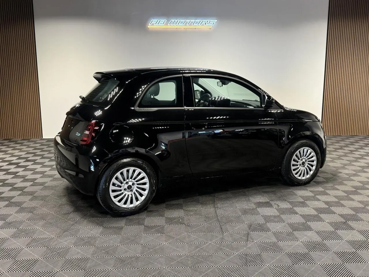Profil droit d'une Fiat 500 électrique noire 2024, avec jantes acier 15 pouces et éclairage LED arrière visible.