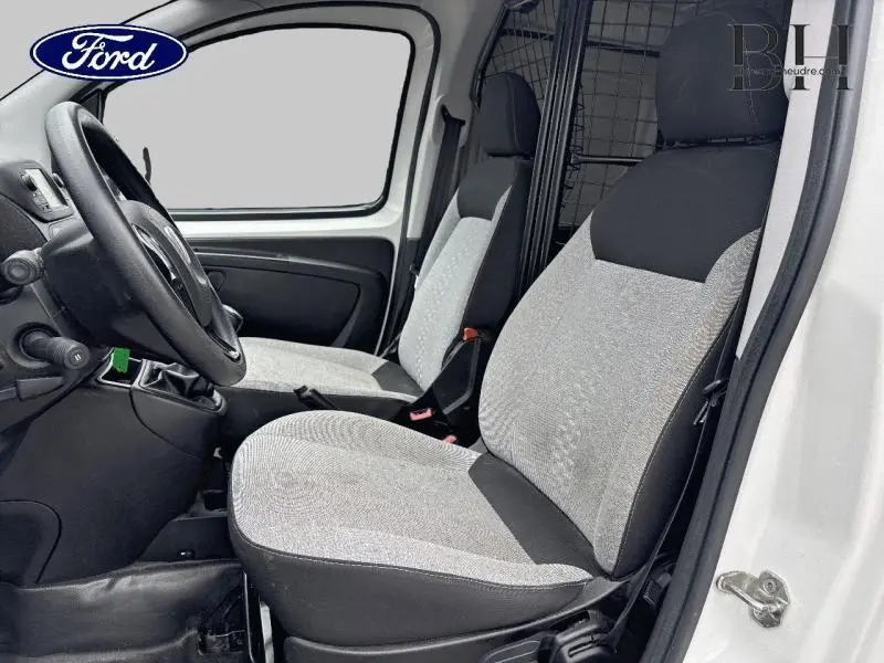 Intérieur côté conducteur d'un utilitaire blanc, sièges gris et noirs avec cloison de protection métallique visible.