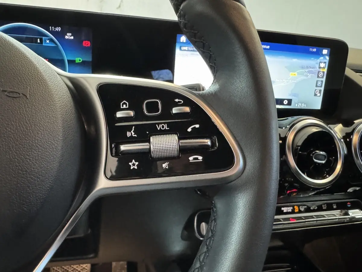 Gros plan sur la partie gauche du volant cuir du Mercedes GLA 250 e gris foncé, avec commandes tactiles et écran tactile en arrière-plan.