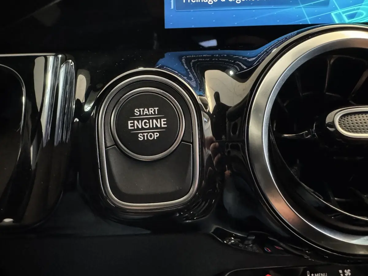 Gros plan sur le bouton Start Engine Stop noir entouré de chrome dans l’habitacle brillant gris foncé d’une Mercedes GLA 250 e Business Line 2023.