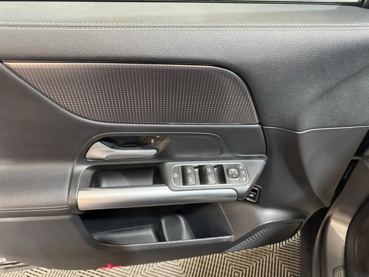 Vue intérieure du panneau de porte avant gauche gris foncé du Mercedes GLA 250 e avec commandes des vitres et poignée argentée.