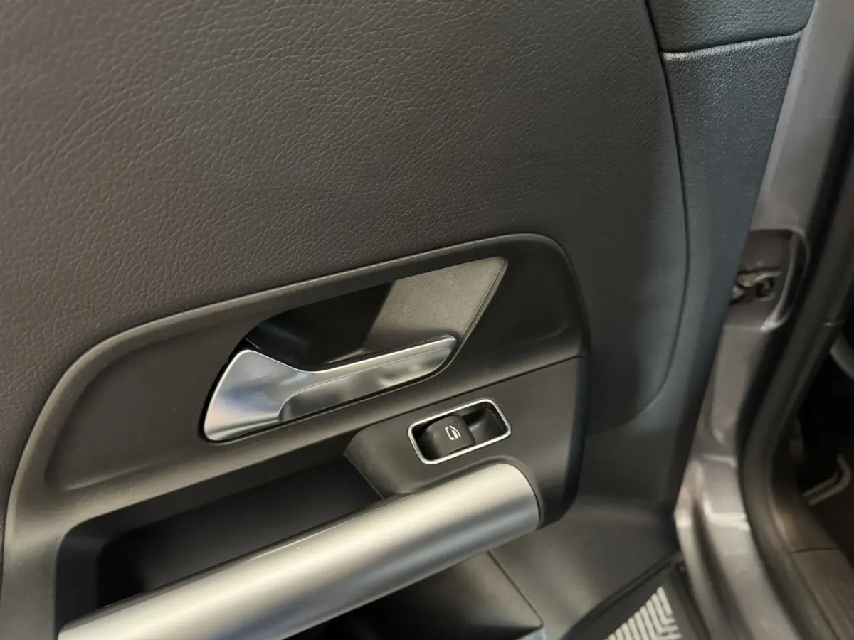 Gros plan sur la poignée intérieure et le bouton de vitre électrique côté droit d’une porte gris foncé de Mercedes GLA 250 e.