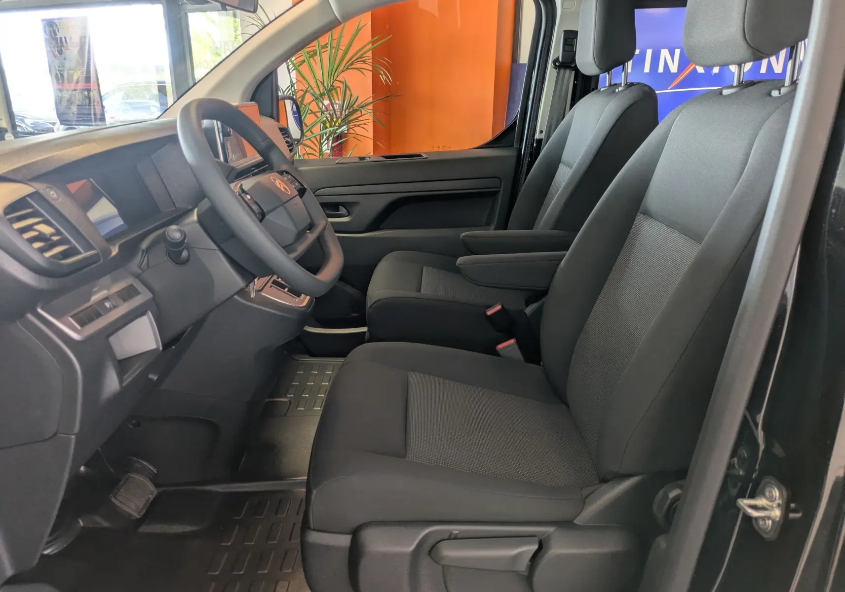 Vue intérieure côté conducteur du Citroën Jumpy cabine approfondie noir, sièges tissu bi-ton gris et noir avec accoudoirs.