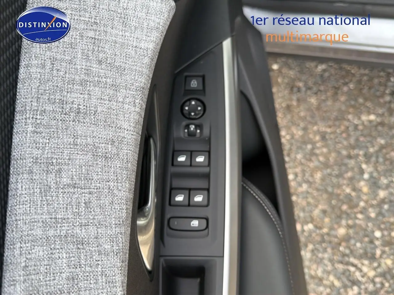 Gros plan sur la commande des vitres électriques et rétroviseurs côté conducteur avec tissu gris et garniture noire.