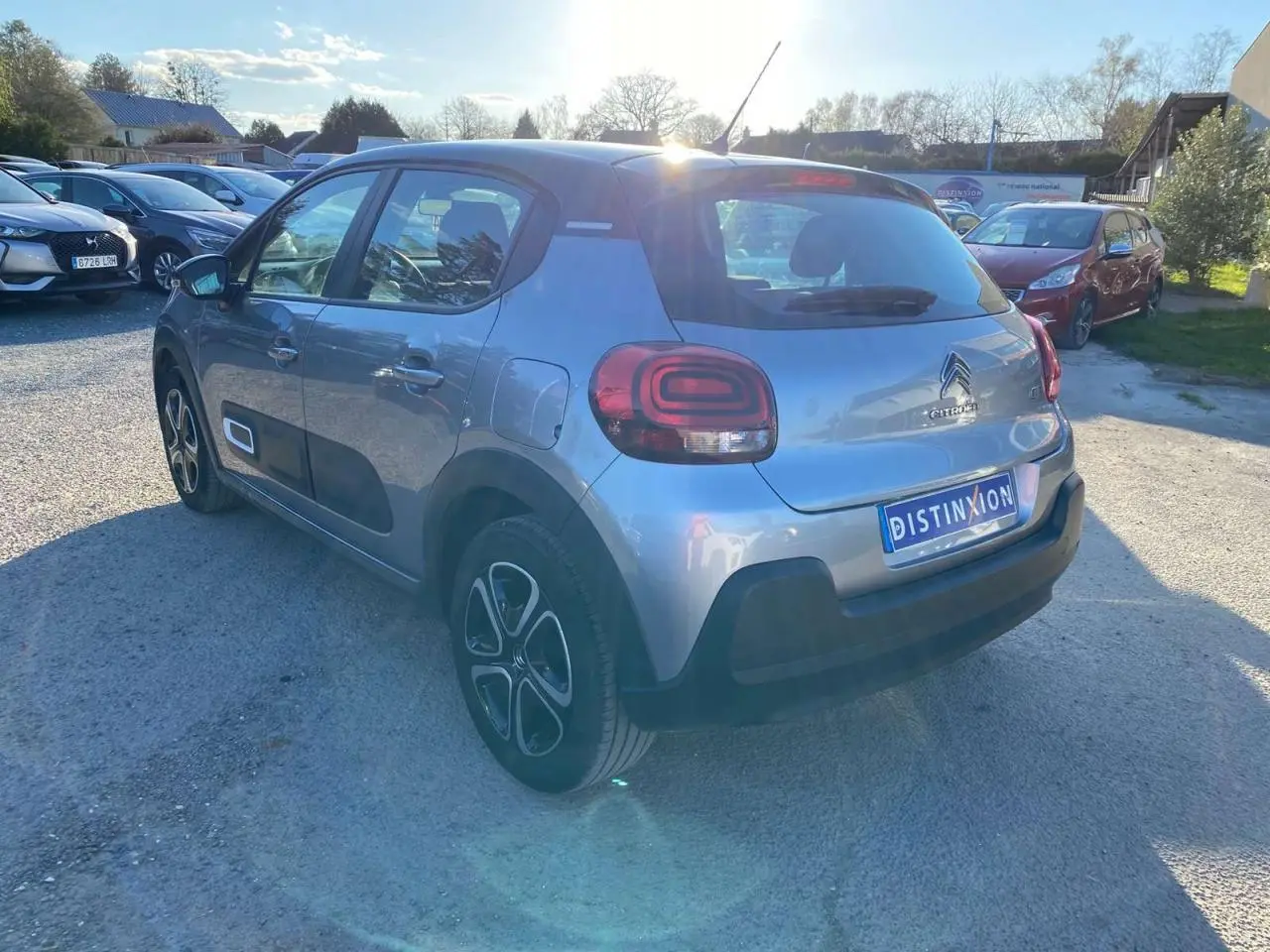 Vue 3/4 arrière droite d'une Citroën C3 gris Artense avec toit noir et protections latérales noires sur un parking.