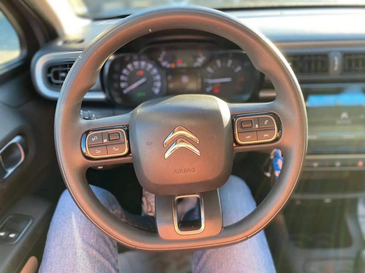 Vue rapprochée du volant noir de la Citroën C3 2022 avec commandes intégrées et tableau de bord flou en arrière-plan.