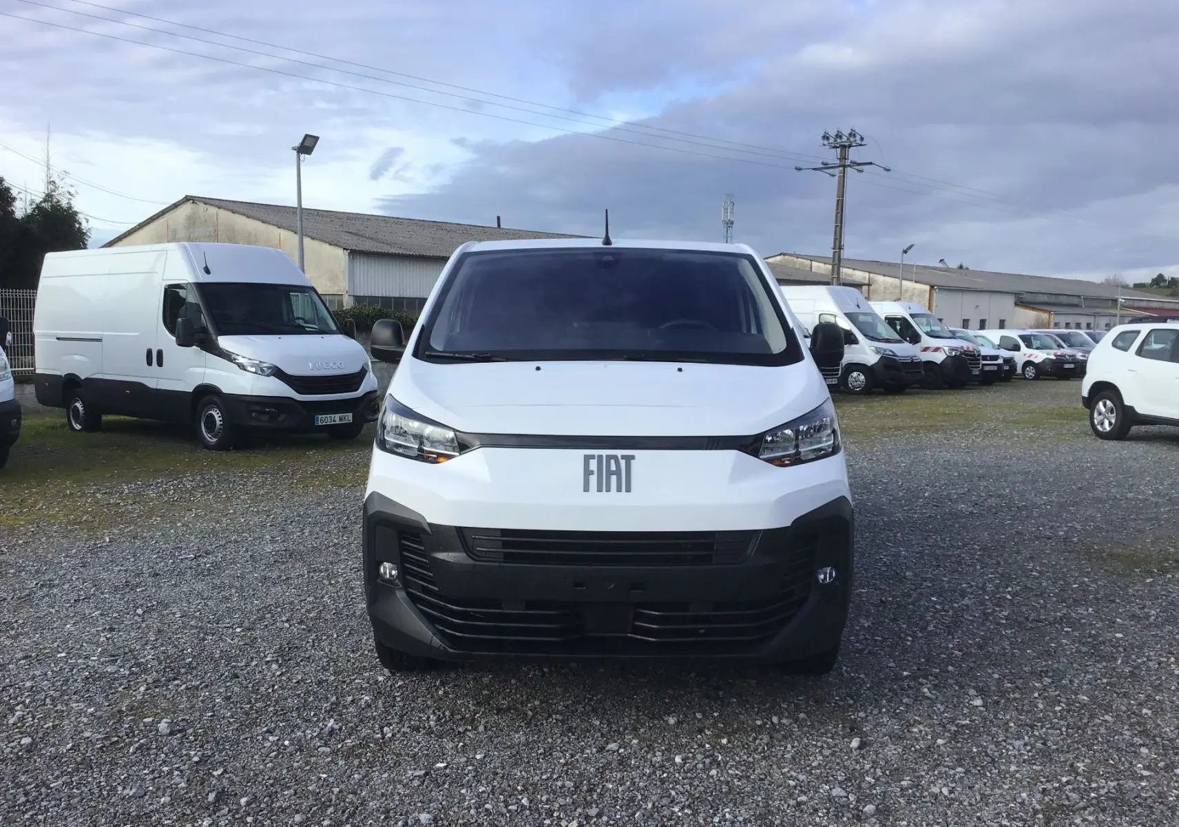 Vue de face d'un FIAT Scudo Fourgon blanc 2024 avec calandre noire et logo FIAT visible sur un parking extérieur.
