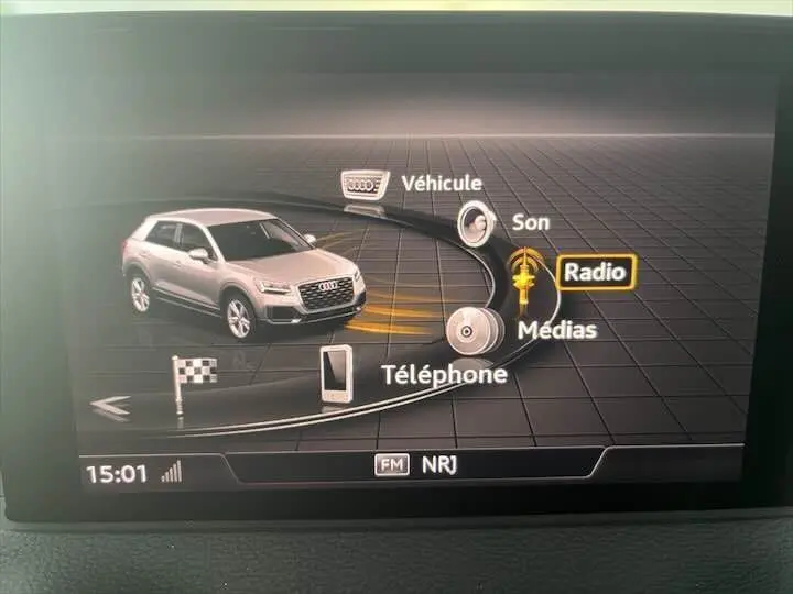 Écran multimédia montrant un Audi Q2 gris Daytona en 3D avec menu radio et options son, médias, téléphone.