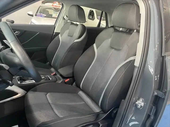 Vue intérieure côté conducteur de l'Audi Q2 gris Daytona, sièges avant en tissu noir avec surpiqûres grises.