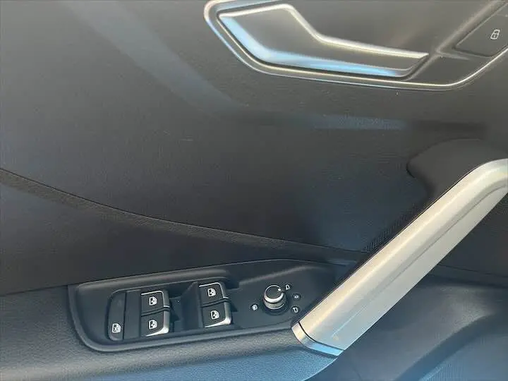 Détail de la porte côté conducteur d'Audi Q2 2020 avec commandes de vitres et rétroviseurs, finition noire et insert argenté.
