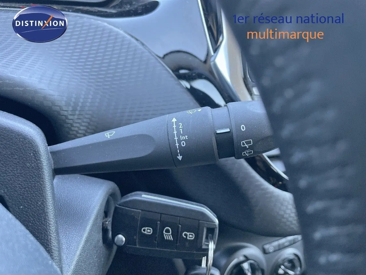 Gros plan sur la commande d'essuie-glace et la clé insérée dans le contact d'un Peugeot 2008 blanc, intérieur sombre.