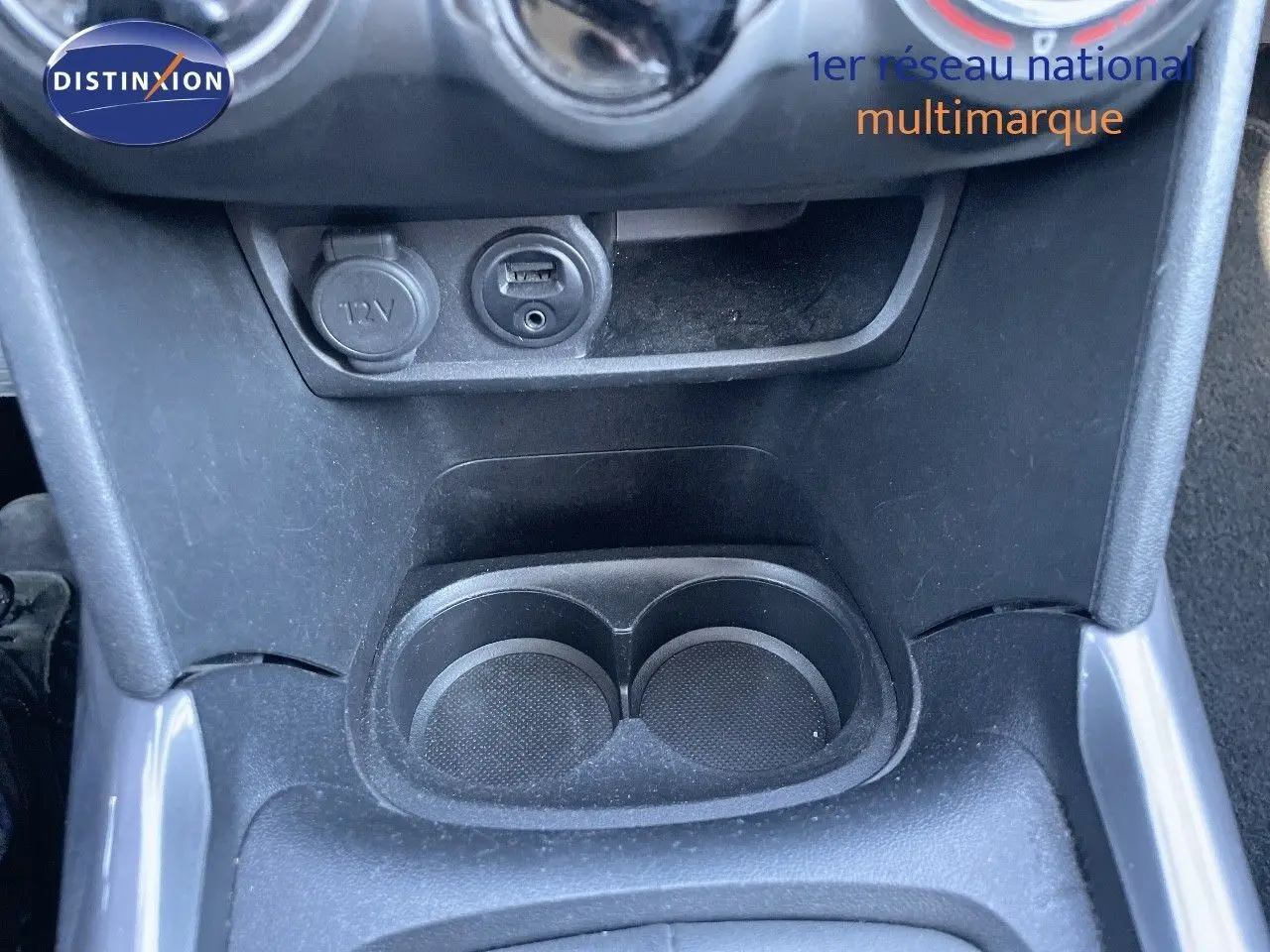 Gros plan sur la console centrale de la Peugeot 2008 blanche, montrant prise 12V, port USB et porte-gobelets noirs.