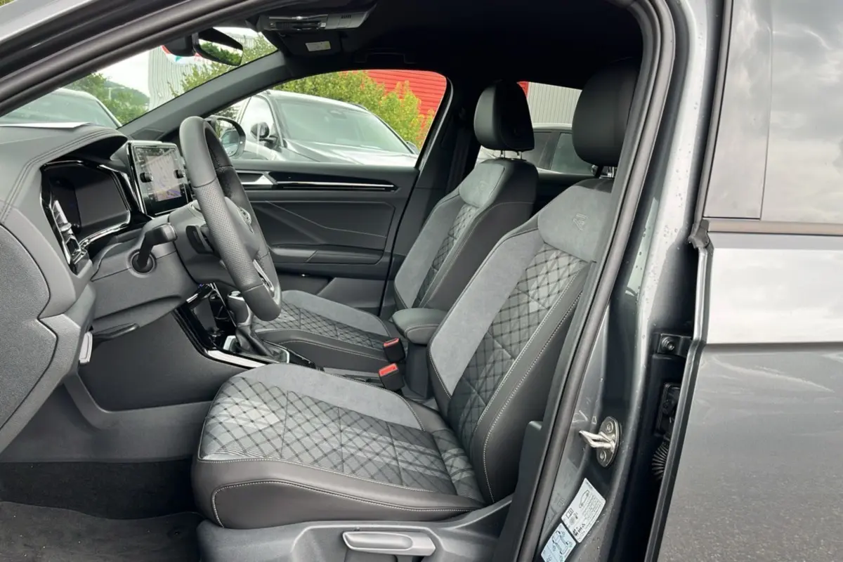 Vue intérieure côté conducteur du Volkswagen T-ROC gris indium 2025, sièges R-Line Black en cuir et alcantara avec surpiqûres.
