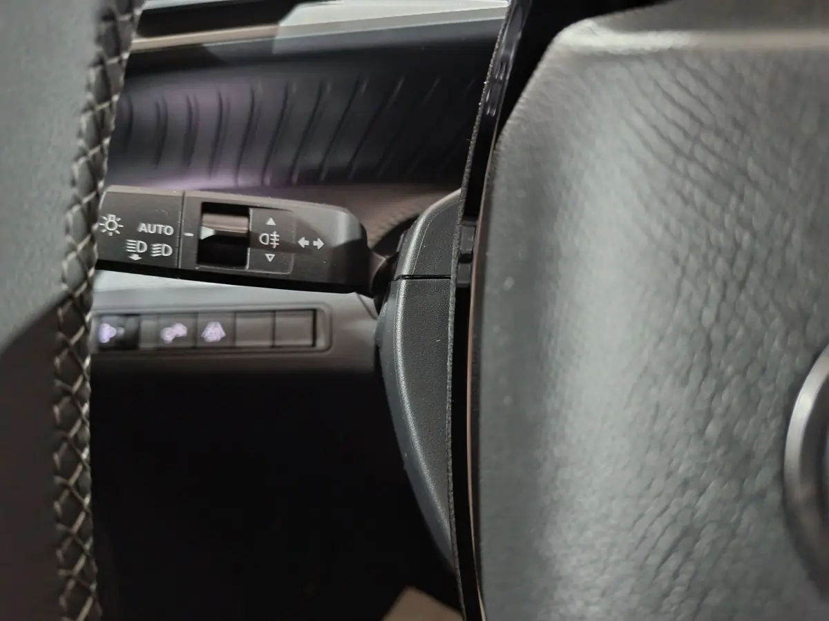 Gros plan sur la manette de commande d'éclairage à gauche du volant cuir noir du Citroën C3 hybride 2025.